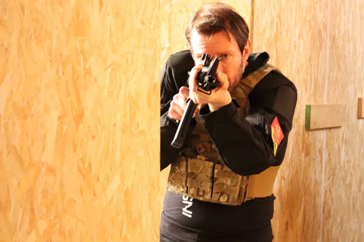Operatore con giubbotto tattico che mira con una pistola T4E dietro un angolo