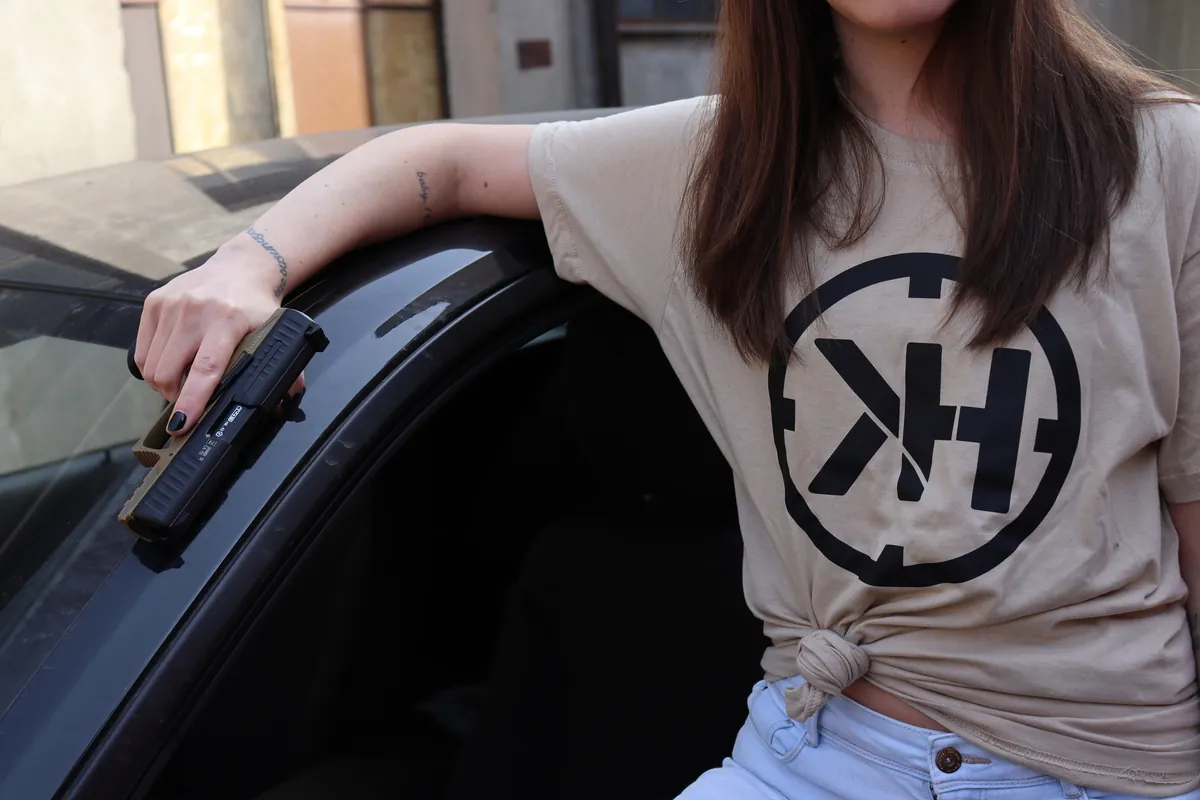 Istruttrice con maglietta Kill House e pistola T4E accanto a un’auto